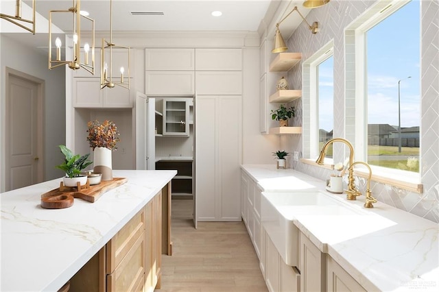 kitchen featuring light stone countertops, sink, light hardwood / wood-style floors, and decorative light fixtures