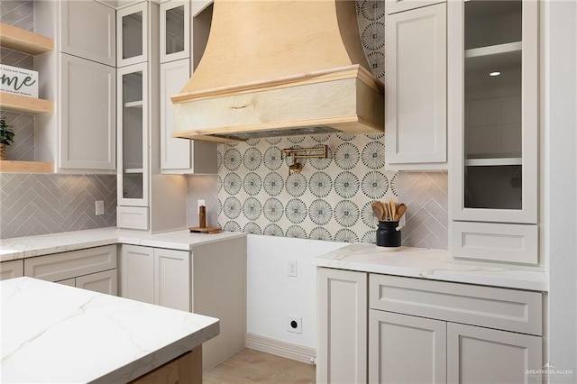 kitchen featuring custom exhaust hood, tasteful backsplash, light stone countertops, and white cabinetry