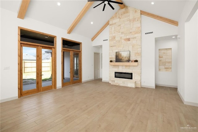 unfurnished living room with french doors, light hardwood / wood-style flooring, beamed ceiling, ceiling fan, and a fireplace