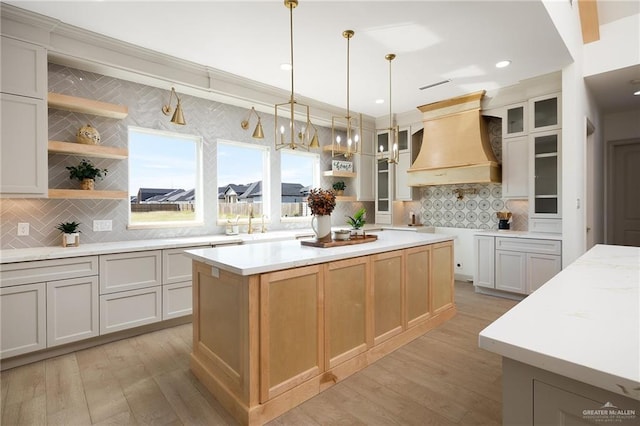 kitchen with white cabinetry, backsplash, a center island, light stone counters, and custom range hood