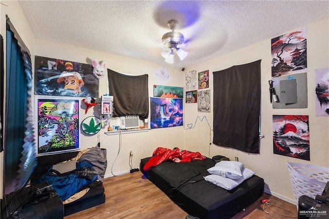 bedroom featuring ceiling fan, hardwood / wood-style floors, cooling unit, and a textured ceiling