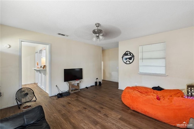 living room with a textured ceiling, ceiling fan, and dark hardwood / wood-style floors