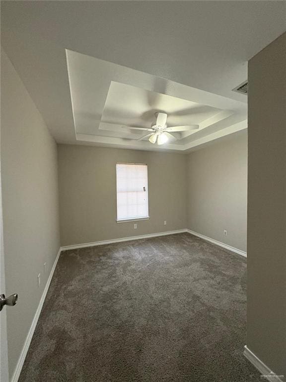 empty room with ceiling fan, dark carpet, and a tray ceiling