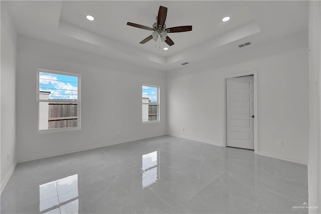 unfurnished room with a raised ceiling, a wealth of natural light, and ceiling fan