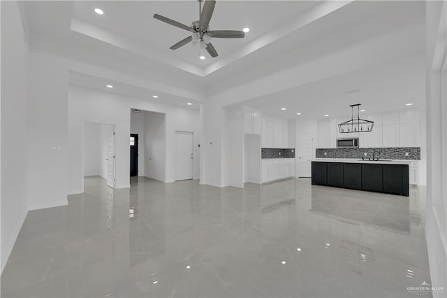 unfurnished living room featuring a raised ceiling, ceiling fan, and sink