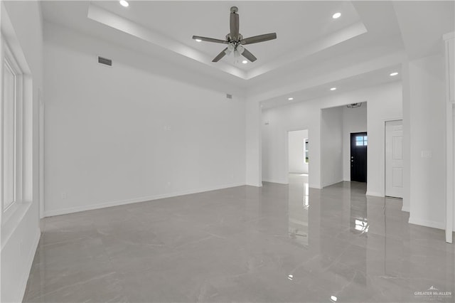 empty room with ceiling fan and a raised ceiling