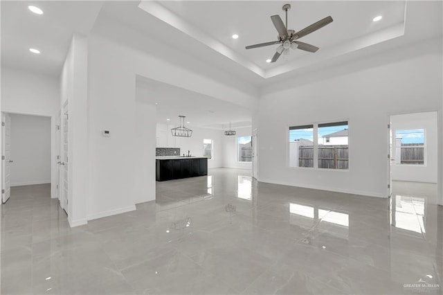 unfurnished living room featuring a tray ceiling, ceiling fan, sink, and a high ceiling