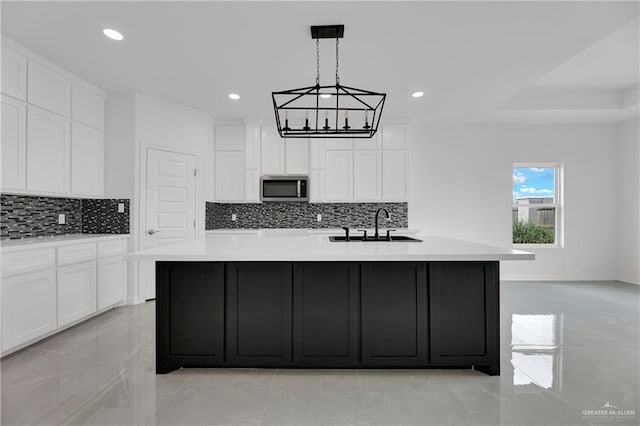 kitchen featuring backsplash, white cabinets, sink, and an island with sink