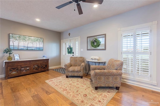 living area with ceiling fan, light hardwood / wood-style floors, a healthy amount of sunlight, and a textured ceiling