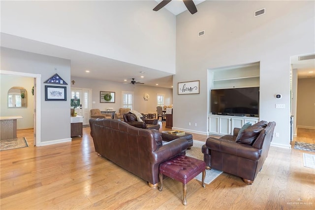 living room featuring ceiling fan, a towering ceiling, and light hardwood / wood-style flooring