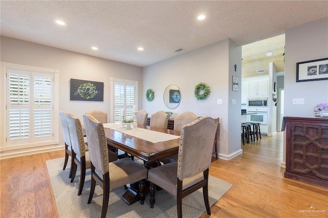 dining area with plenty of natural light, a textured ceiling, and light hardwood / wood-style flooring