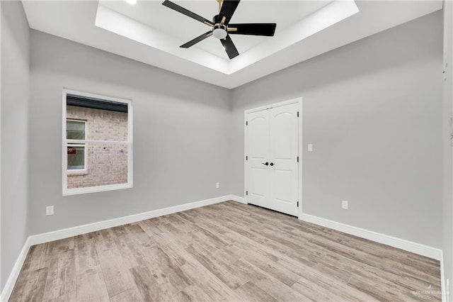 unfurnished room with ceiling fan, a tray ceiling, and light hardwood / wood-style flooring