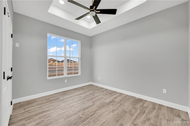 unfurnished room with ceiling fan, a tray ceiling, and light hardwood / wood-style floors