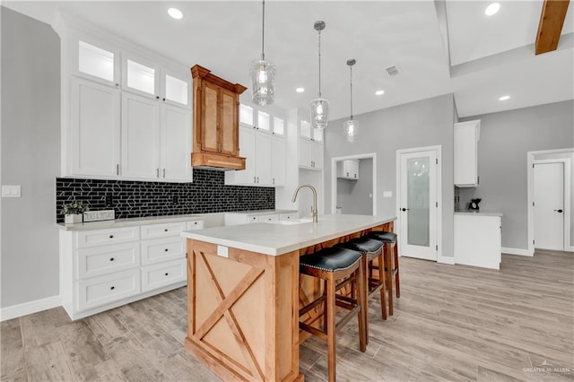 kitchen featuring sink, light hardwood / wood-style flooring, an island with sink, white cabinets, and decorative light fixtures