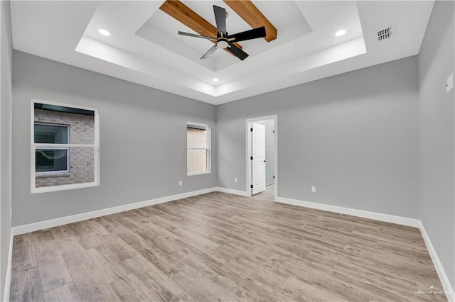 unfurnished room with ceiling fan, a tray ceiling, and light wood-type flooring