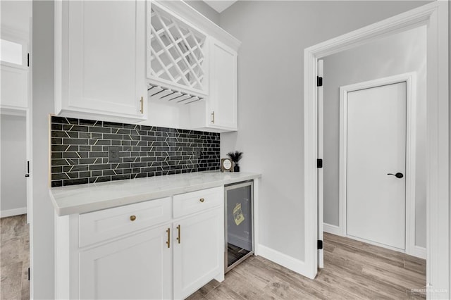 kitchen featuring white cabinetry, backsplash, light stone countertops, light hardwood / wood-style floors, and beverage cooler