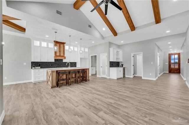 kitchen with beamed ceiling, white cabinetry, hanging light fixtures, a center island with sink, and light hardwood / wood-style flooring