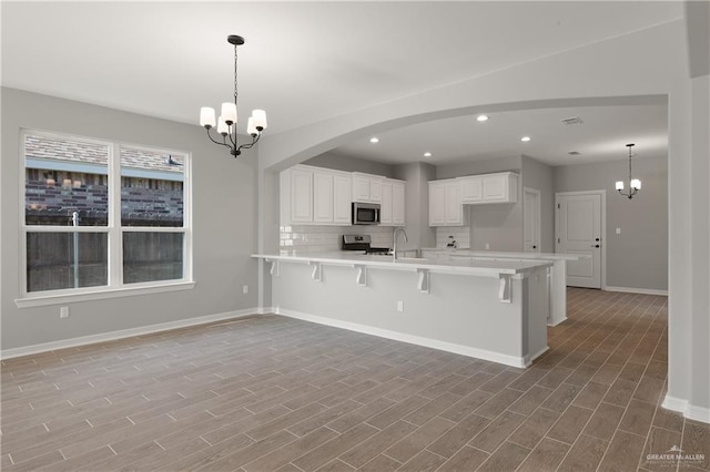 kitchen with a kitchen bar, stainless steel appliances, hanging light fixtures, and white cabinets