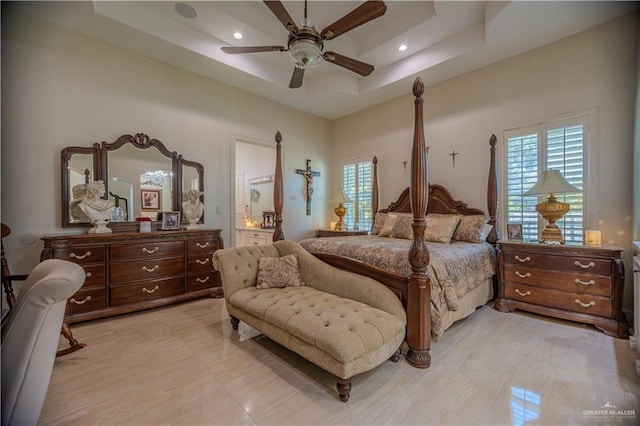 bedroom featuring a ceiling fan, a raised ceiling, ensuite bath, and multiple windows