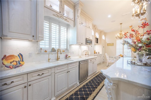kitchen with a sink, stainless steel appliances, a chandelier, backsplash, and white cabinetry