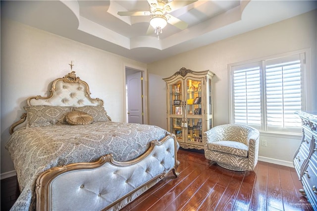 bedroom with a tray ceiling, baseboards, hardwood / wood-style floors, and a ceiling fan