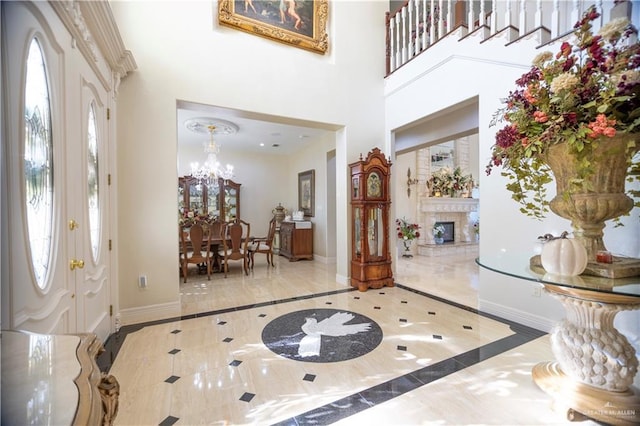 foyer entrance with a notable chandelier, baseboards, a high ceiling, and a glass covered fireplace