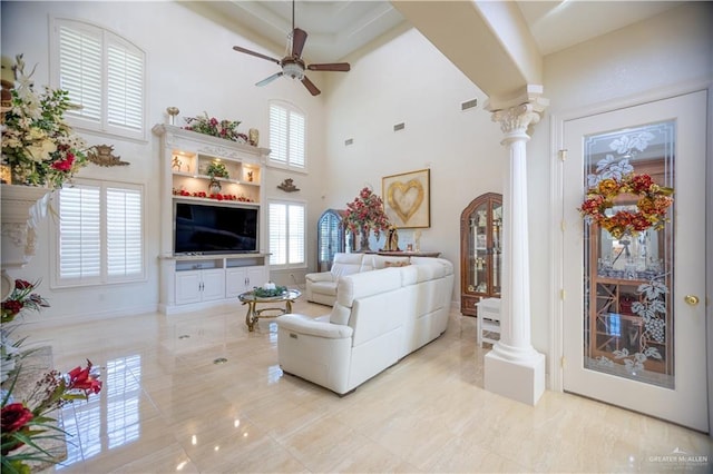 living area featuring ceiling fan, a towering ceiling, visible vents, and decorative columns