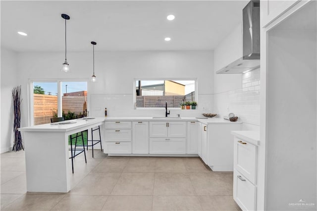 kitchen featuring wall chimney range hood, backsplash, light countertops, a peninsula, and recessed lighting