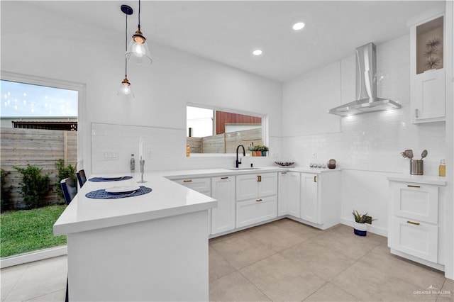 kitchen featuring a sink, wall chimney exhaust hood, a peninsula, and decorative backsplash