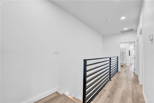 corridor with visible vents, light wood-style flooring, baseboards, and an upstairs landing