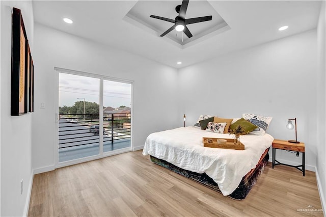 bedroom with wood finished floors, access to exterior, baseboards, ceiling fan, and a tray ceiling
