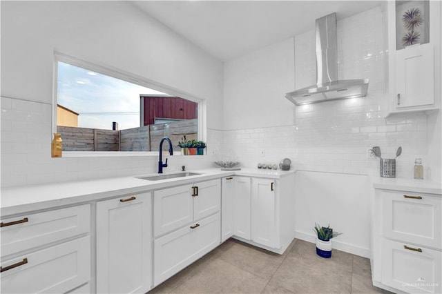 kitchen featuring a sink, wall chimney exhaust hood, white cabinetry, decorative backsplash, and light tile patterned floors