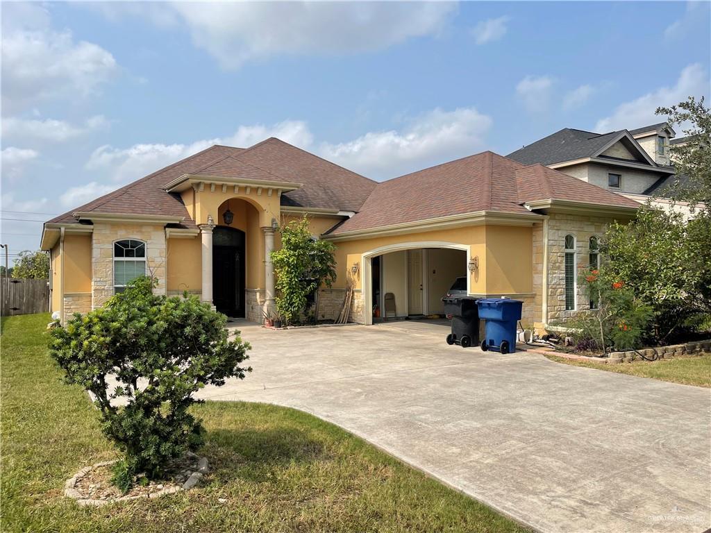 mediterranean / spanish-style house featuring a garage, concrete driveway, stone siding, roof with shingles, and a front lawn