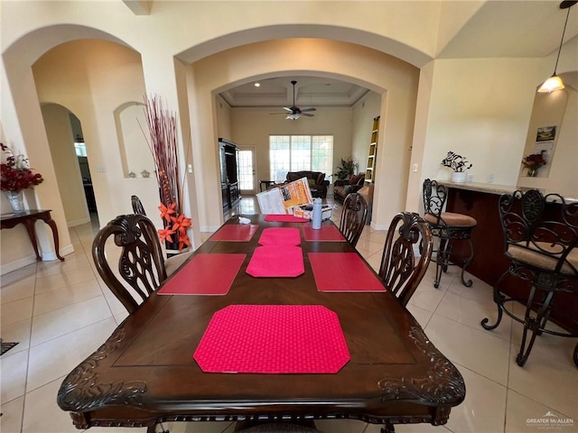 dining area featuring arched walkways, light tile patterned flooring, ceiling fan, and baseboards