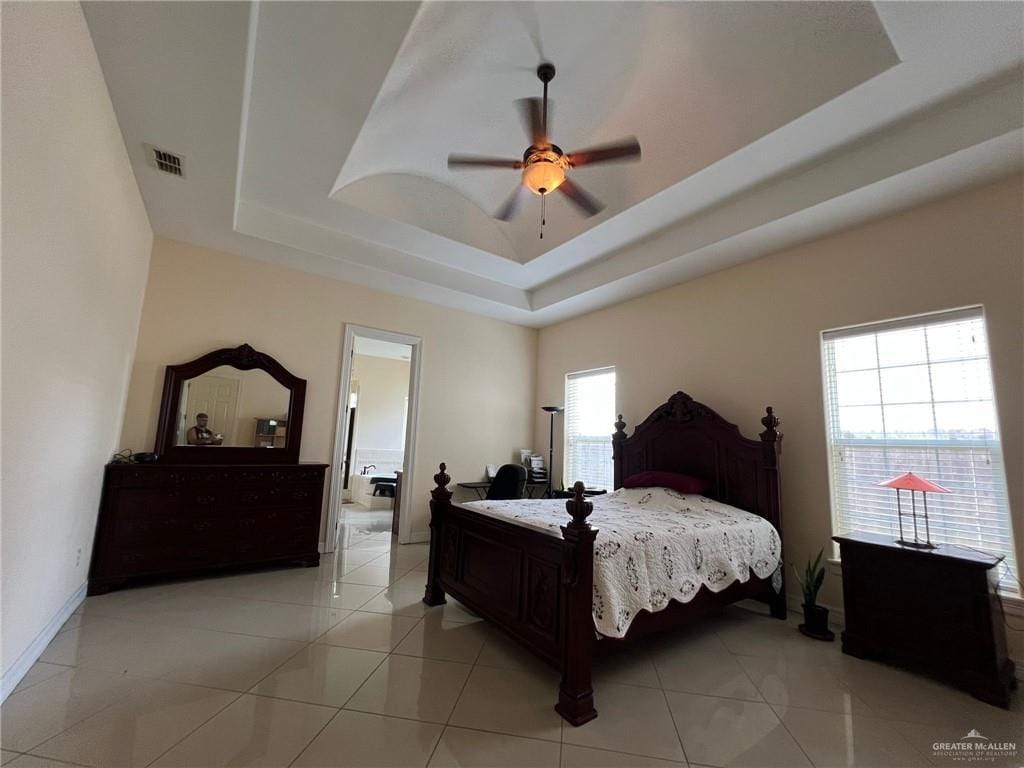 bedroom featuring light tile patterned floors, ceiling fan, visible vents, baseboards, and a tray ceiling