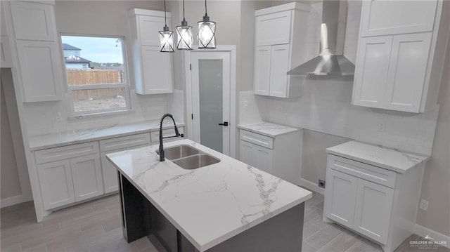 kitchen featuring a kitchen island with sink, sink, wall chimney exhaust hood, and pendant lighting