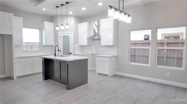 kitchen with a wealth of natural light, wall chimney exhaust hood, sink, a center island with sink, and white cabinets