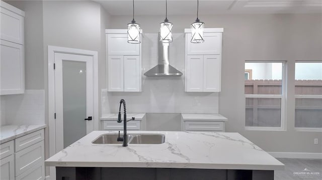 kitchen featuring white cabinets, light stone counters, sink, and an island with sink