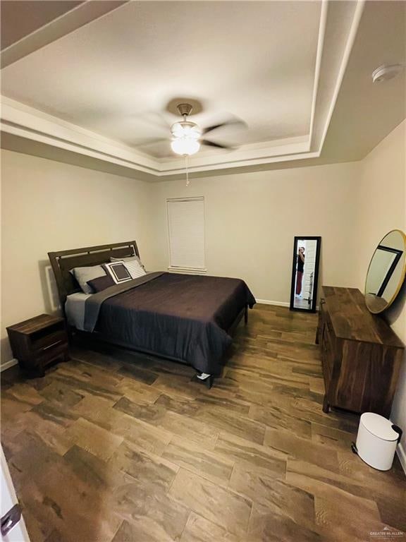 bedroom with ceiling fan, a raised ceiling, and wood-type flooring