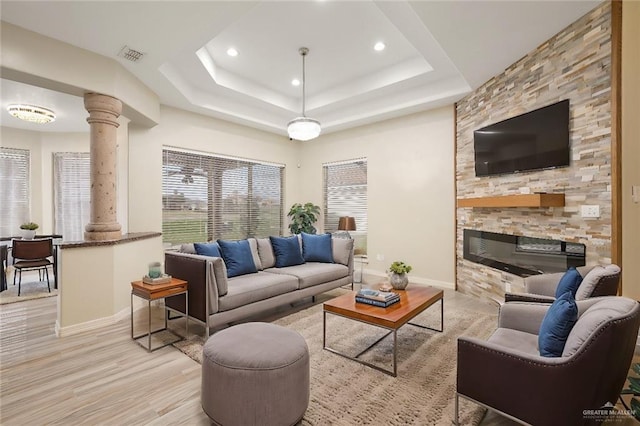 living room featuring light wood-style flooring, visible vents, baseboards, a tray ceiling, and decorative columns