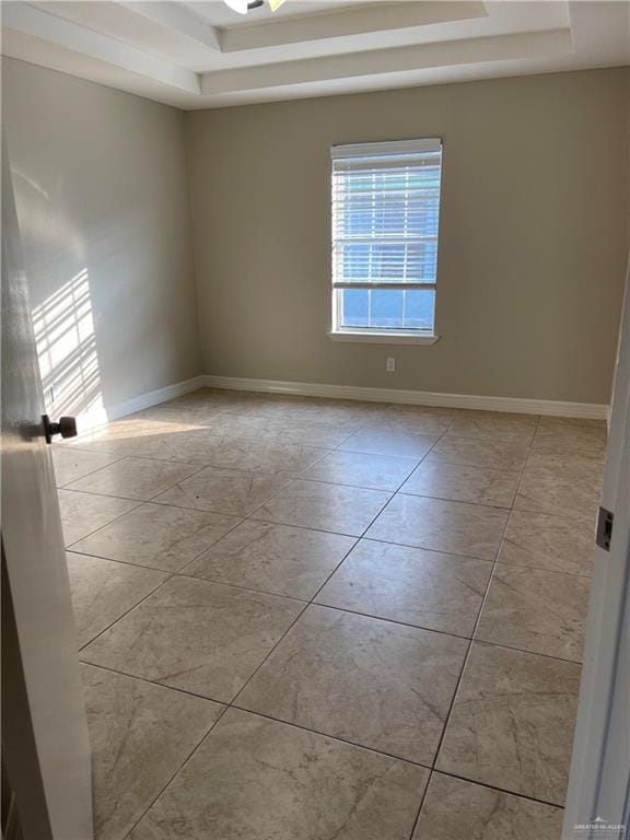 empty room featuring a tray ceiling and baseboards