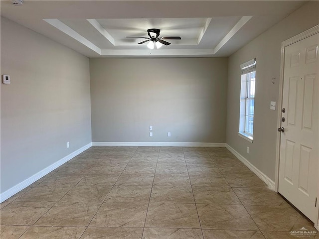 empty room with a raised ceiling, a ceiling fan, and baseboards