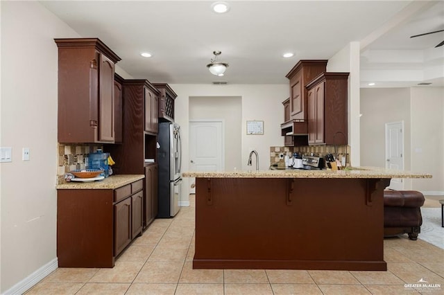 304 N 18th St, Hidalgo, TX 78557 - kitchen with freestanding refrigerator, a peninsula, a kitchen breakfast bar, decorative backsplash, and light stone countertops