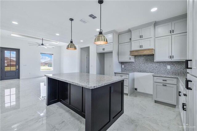 kitchen with tasteful backsplash, marble finish floor, a kitchen island, light stone counters, and visible vents