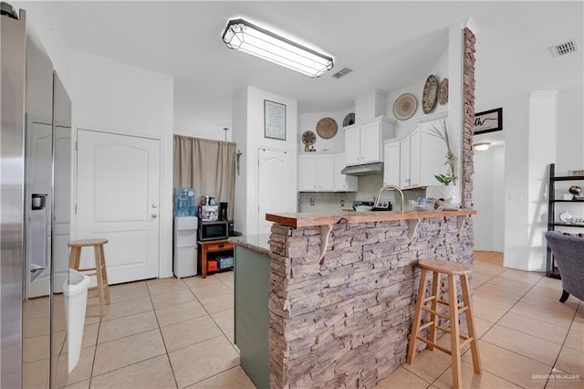 kitchen with visible vents, under cabinet range hood, a kitchen breakfast bar, a peninsula, and light tile patterned flooring