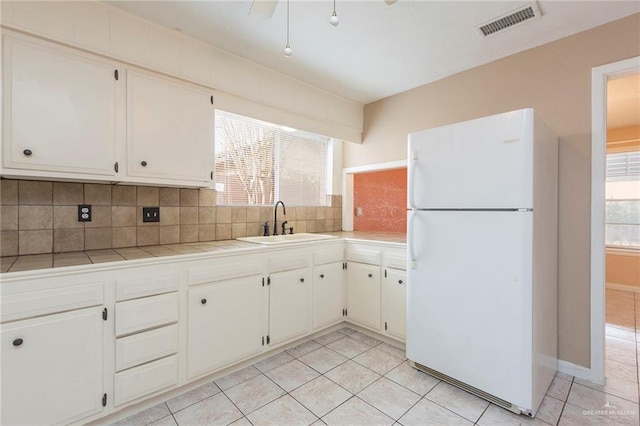 kitchen featuring sink, tile counters, white cabinets, and white refrigerator