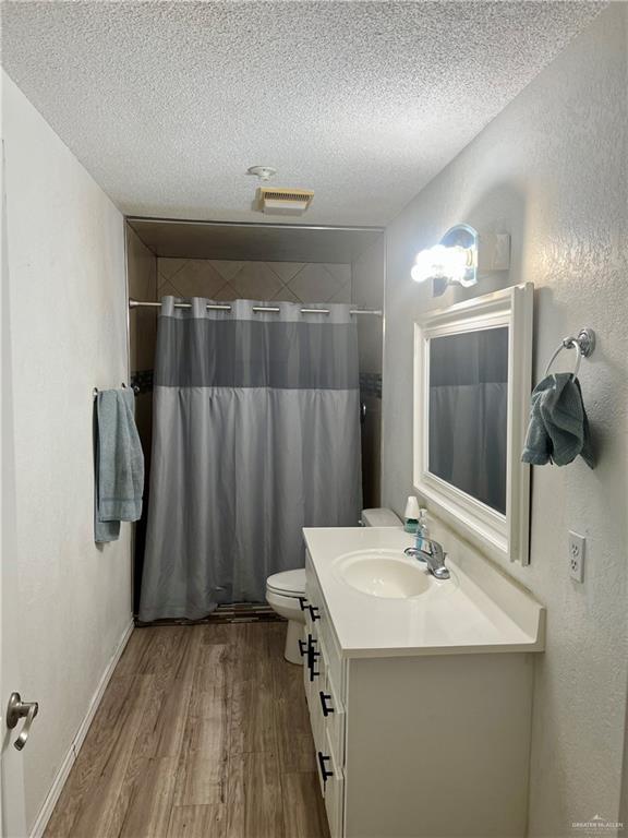 bathroom with toilet, a shower with curtain, a textured ceiling, vanity, and hardwood / wood-style flooring