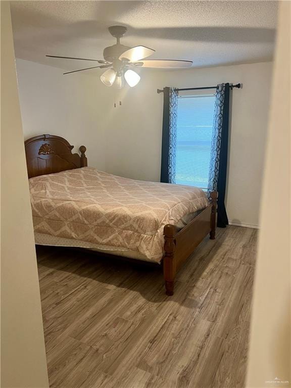 bedroom with ceiling fan, wood-type flooring, and a textured ceiling