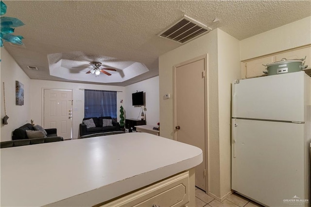 kitchen with ceiling fan, light tile patterned floors, a textured ceiling, a tray ceiling, and white fridge