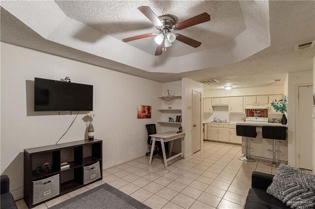 living room with a textured ceiling, a raised ceiling, ceiling fan, sink, and light tile patterned floors